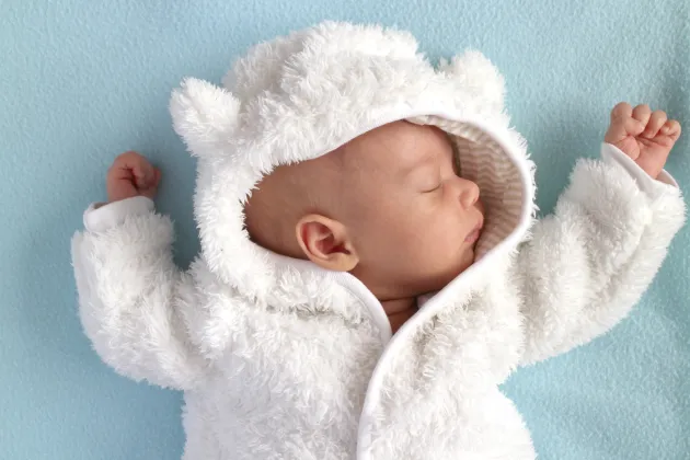 Sleeping cute baby in a white onepiece against blue background, photography. Photo: iStock