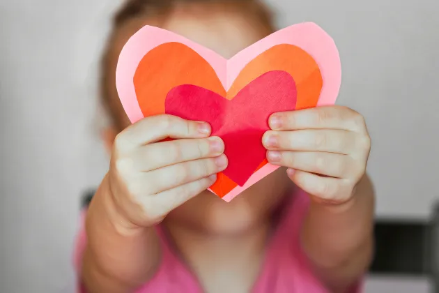 A child holds a paper cut heart in front of her/him. Photo: iStock
