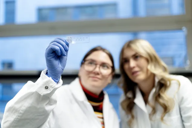 Two students holding up and looking at a lab sample. Photo.